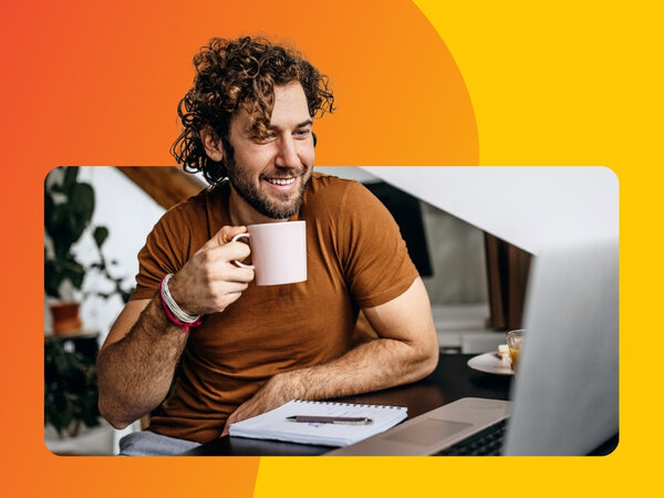 Mann mit halblangen Haaren sitzt vor einem Laptop und hält eine Tasse Kaffee in der Hand.