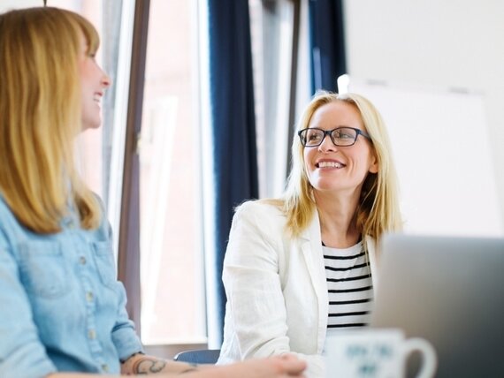 Zwei Frauen im Büro unterhalten sich fröhlich.