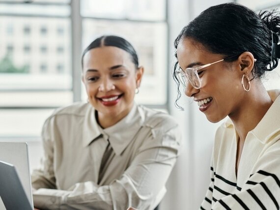 Zwei Frauen mit Laptops. Zwei Frauen arbeiten fröhlich an ihren Laptops.
