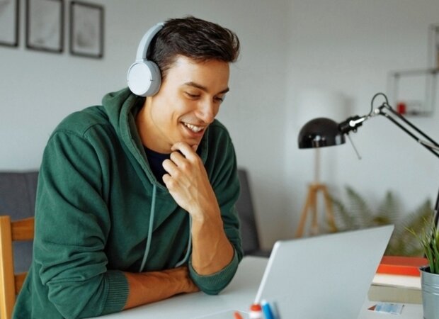 Ein Mann mit Kopfhörern im Homeoffice sitzt vor seinem Laptop.