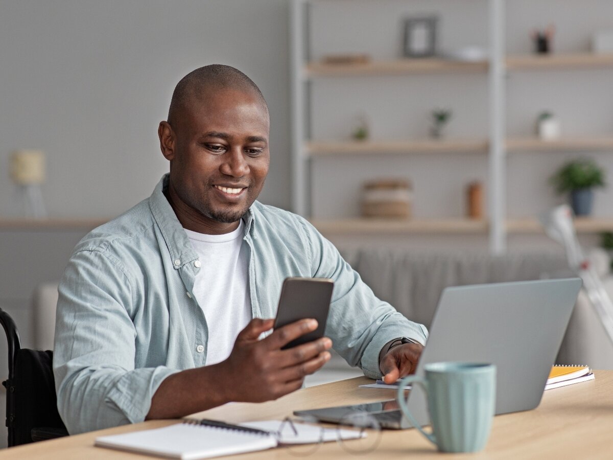 Mann mit Laptop und Smartphone. Ein Mann im Homeoffice arbeitet an seinem Laptop und schaut auf sein Smartphone.