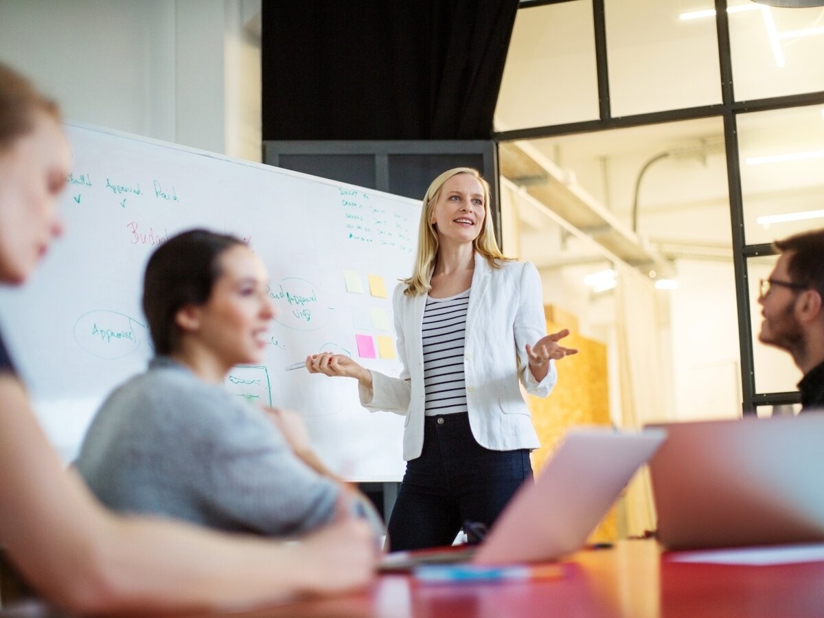 Frau am Whiteboard Eine junge, selbstbewusste Frau steht an einem Whiteboard und erklärt ihrem Team ihre Ideen