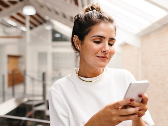 Eine junge Frau schreibt eine Nachricht mit ihrem Smartphone.