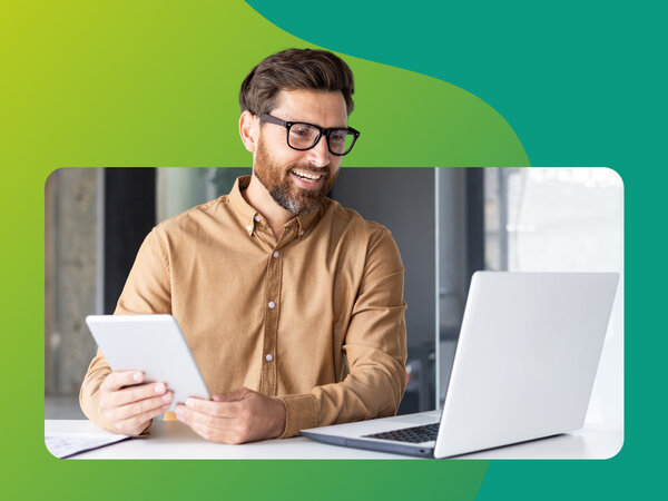 Mann sitzt vor Laptop und hat ein Tablet in der Hand