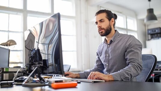 Ein Mann sitzt im Büro am Schreibtisch und arbeitet am Computer