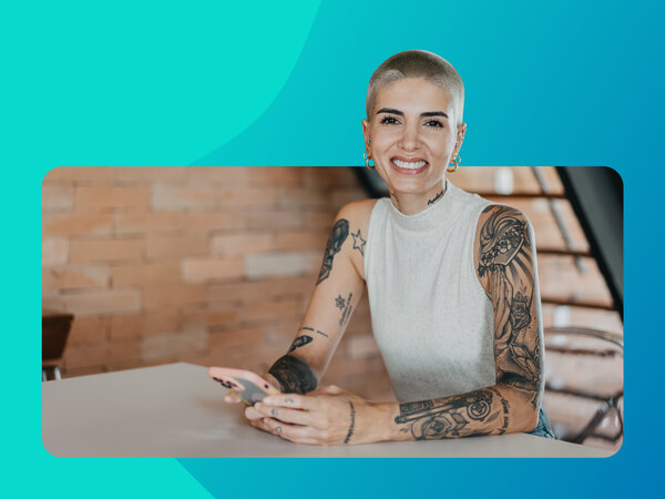 Lächelnde junge Frau mit kurzen Haaren sitzt mit Smartphone in modernem Büro.