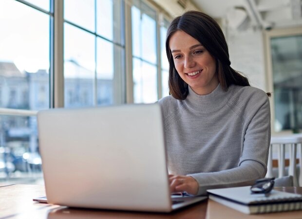 Eine Frau arbeitet am Laptop in einem Büro mit großem Fenster.